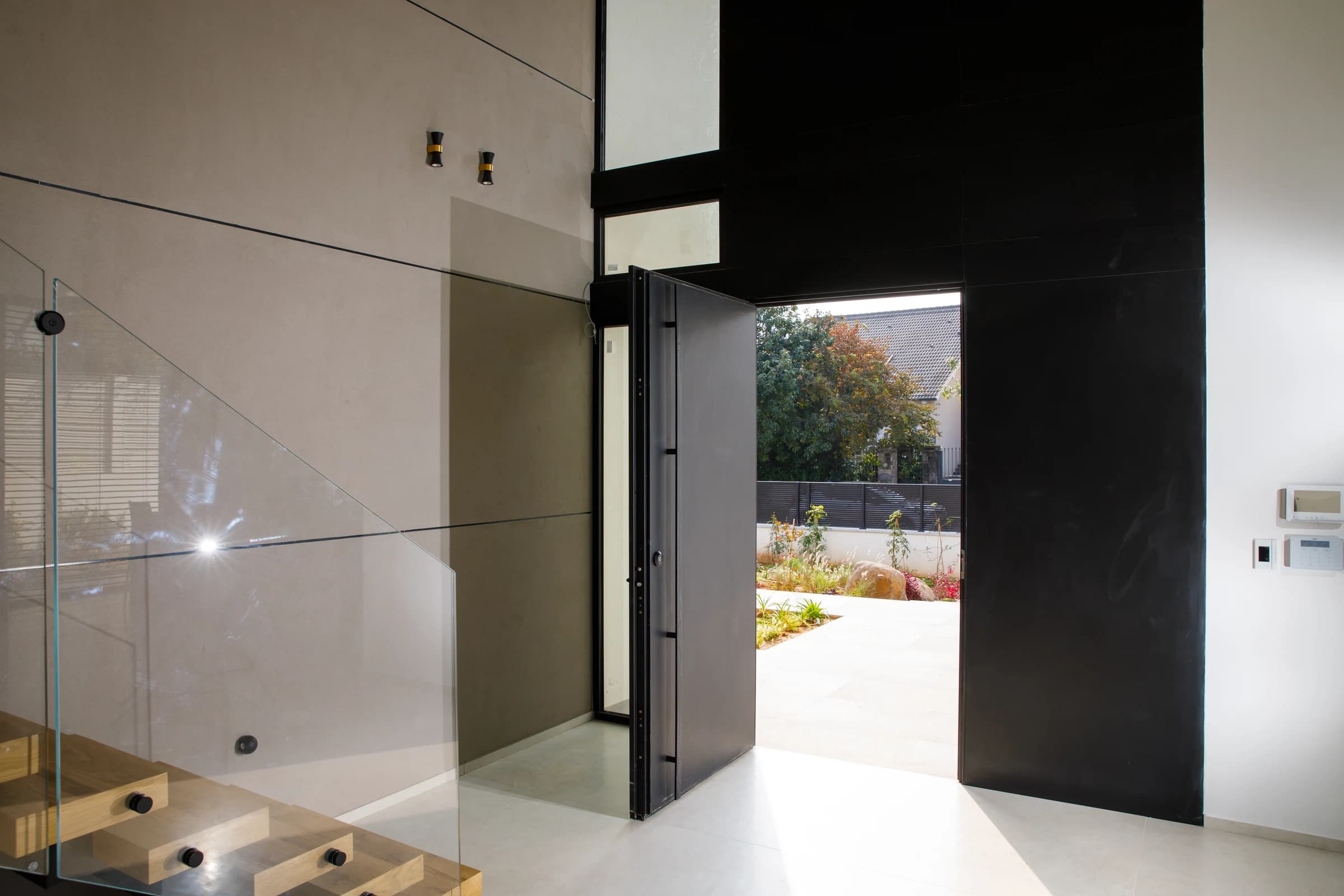 Original Hermetix installation photograph: tall dark entrance door opened to a daylight garden, beside a glass stair rail